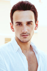 Portrait of a handsome young man in a white shirt. Perfect hair & skin. Summer vacation concept. Outdoor shot.