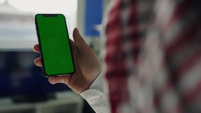 Man is relaxing on comfortable couch and using vertically blank chromakey touchscreen smartphone at home. Focus on phone. Blurred image of national costume, arabic scarf. Business texting, devices