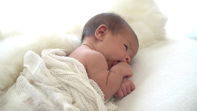4K Selective focus side view medium close up shot of asian female newborn baby lying down on white bed. Cute infant toddler looking around with moving head and hands.