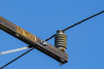 Obraz premium Close up of high voltage distribution line running over a large ceramic insulator. Deep blue sky.