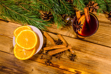 Cup of mulled wine with cinnamon, sliced orange and fir tree branches on wooden table. Top view