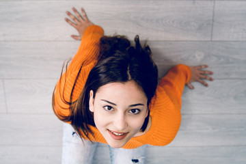 High angle view of beautiful young woman in orange sitting on the floor looking up to the camera