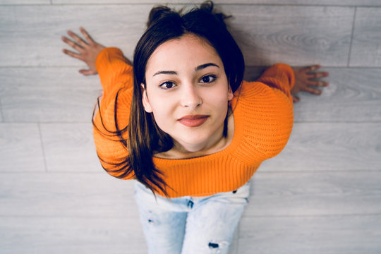 High angle view of beautiful young woman in orange sitting on the floor looking up to the camera