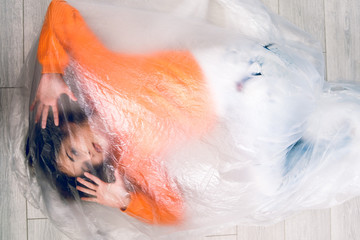 Young woman wrapped in nylon transparent bag trapped frustrated freedom human trafficking concept