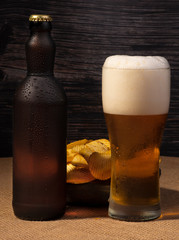 Cold  beer bottle, chips and beer with foam in glass