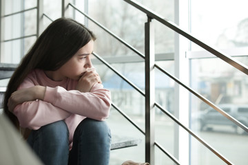 Upset teenage girl sitting on stairs indoors. Space for text