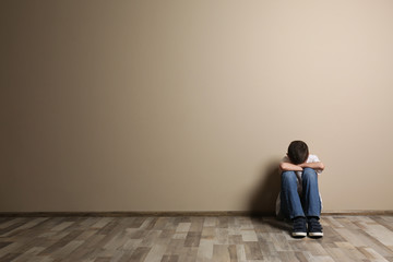 Upset boy sitting on floor at color wall. Space for text