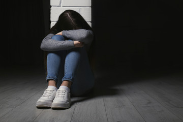 Upset teenage girl sitting at column indoors. Space for text