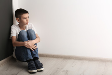 Upset boy sitting on floor indoors. Space for text