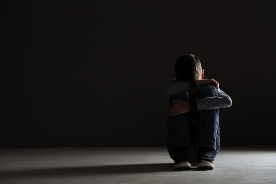 Upset Boy Sitting In Dark Room. Space For Text