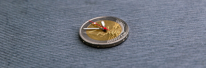 enrichment time: 2 euro coin with hour hands on a dark background, short focus, close