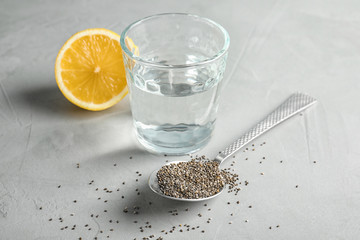 Spoon with chia seeds and glass of water on grey background
