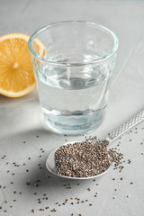 Spoon with chia seeds and glass of water on grey background