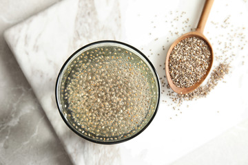 Glass of water with chia seeds and spoon on board, top view