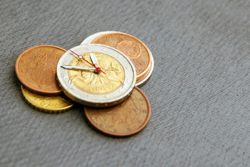 time to benefit: 2 euro coin with hour hands on other money against a dark background, short focus, close