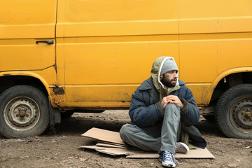 Poor homeless man sitting near van outdoors - obrazy, fototapety, plakaty