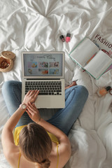 Woman and laptop with open cooking blog on bed, top view