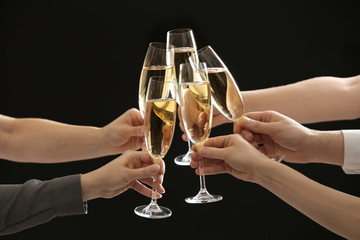 People clinking glasses of champagne on dark background, closeup
