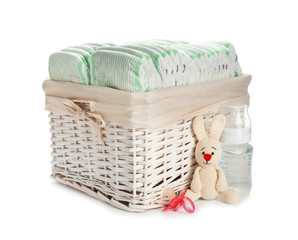 Wicker basket with disposable diapers and baby accessories on white background