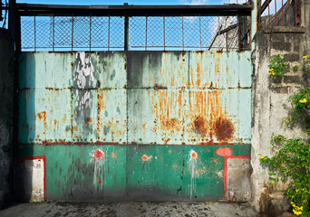 Colorful old rusty entrance metal gate pictured in Iloilo City, Philippines, at daytime. Located behind the gate is an industrial entity.