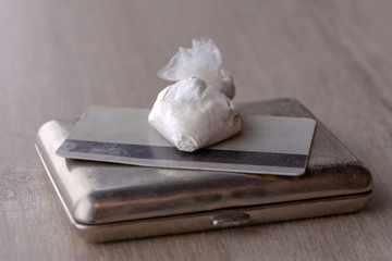 dose of cocaine in a plastic bag and a card on an old cigarette case