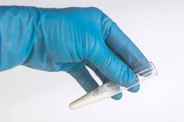 detection of cocaine and heroin: a medical laboratory worker holds in his hand a test tube with a sample of a powder of narcotic substance for analysis, on a white background