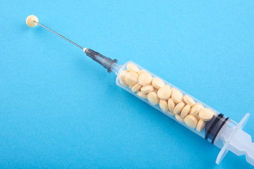 Syringe filled with yellow pills on blue background