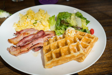 American breakfast consist of homemade bacon, waffles, salad and scrambled egg