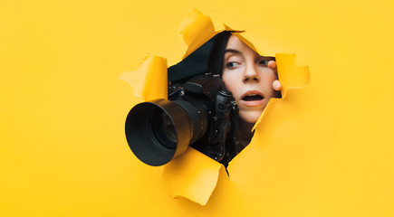 A young paparazzi girl with a reflex camera looks out from cover and looks at what is happening...