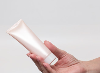 Female hand holding a cream tube, white background. Skin care product. Health and beauty concept. Front view. 
