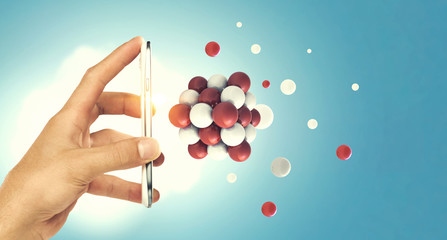 Businessman hand holding a smartphone with a bunch of spheres levitating beside. Mixed media