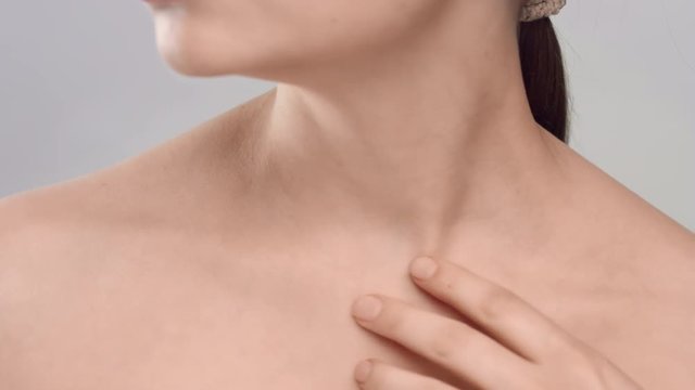 Woman gently strokes her clavicles on light grey background