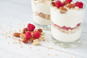 Two glasses of greek yogurt granola with raspberries, oatmeal flakes and nuts on a white background. Healthy nutrition