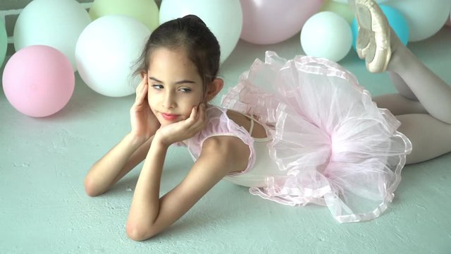4K Video selective focus side view dolly shot of young beautiful ballerina girl in pink leotard and tutu costume lying down on the floor and perform stretching her leg for flexibility muscular.
