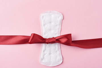 Sanitary pad and red ribbon on a pink background
