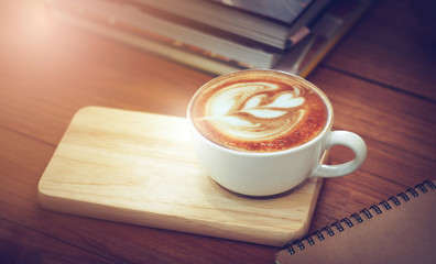 Closeup of latte art coffee on wooden table with book and note background, vintage color tone