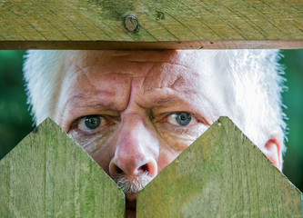 A curious man is watching over a wooden fence. Concept curiosity.