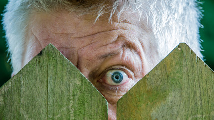 A curious man is watching over a wooden fence. Concept curiosity.