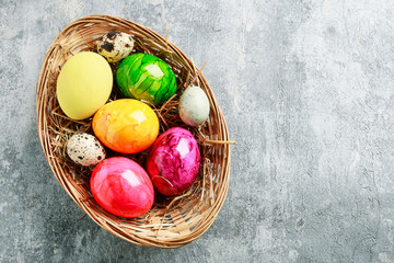 Basket of colorful Easter eggs on grey, stone background.