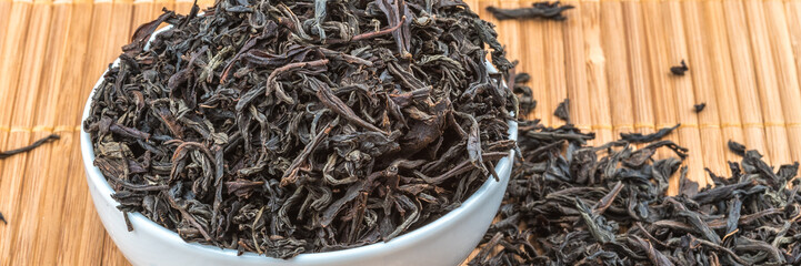Dried tea is poured into a ceramic cup on a bamboo mat.
