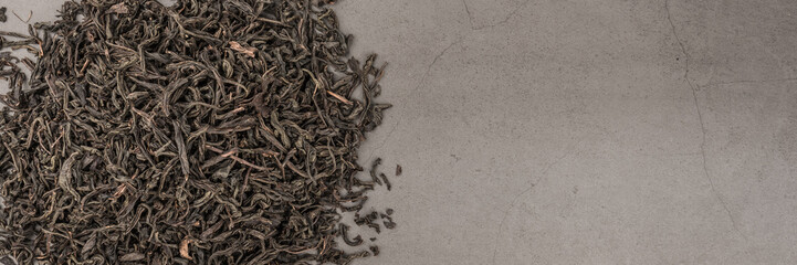 Dried tea is poured scattered on a grey textured background.