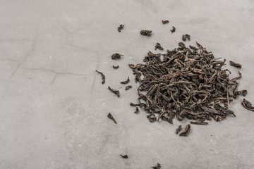 Dried tea is poured scattered on a grey textured background.