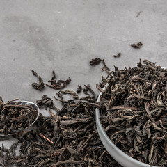 Dried tea in a white ceramic cup with a spoon on a gray textured background.