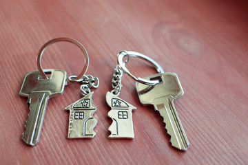 Two keys with splitted or broken key rings with pendant in shape of house divided in two parts on wooden background with copy space. Dividing house when divorce, division of property, real estate heri