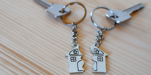 Two keys with splitted or broken key rings with pendant in shape of house divided in two parts on wooden background with copy space. Dividing house when divorce, division of property, real estate heri