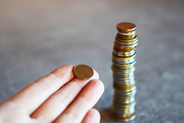 Two cent euro coin in hand next to stock of money coins on grey table with copy space. Personal...