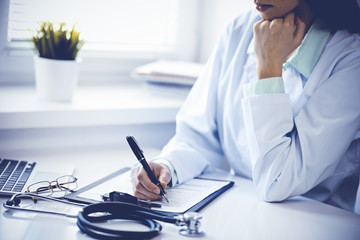 Doctor woman working with medication history records form while sitting at the desk near window in hospital. Medicine and health care concept. Green is main color