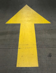 A painted, yellow, up arrow is shown on the ground surface of a parking garage.