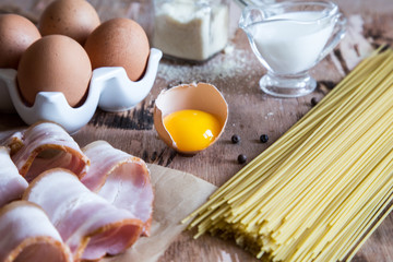 Ingredients for Pasta Carbonara with bacon, cheese, cream and yolk on wooden table. Preparing Spaghetti alla carbonara.
