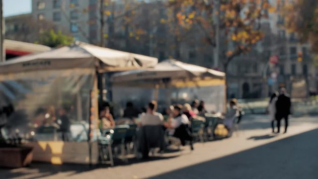 A group of friends relaxing, sitting at an outside cafe patio under a tent, in a city, enjoying the mild temperature of the day. Blurred shot.